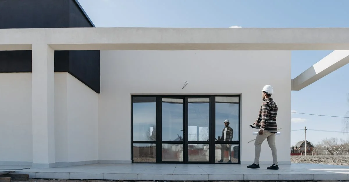 Architecte avec casque de sécurité évaluant l'extérieur moderne d'une maison. Idéal pour des thèmes de construction et d'architecture.