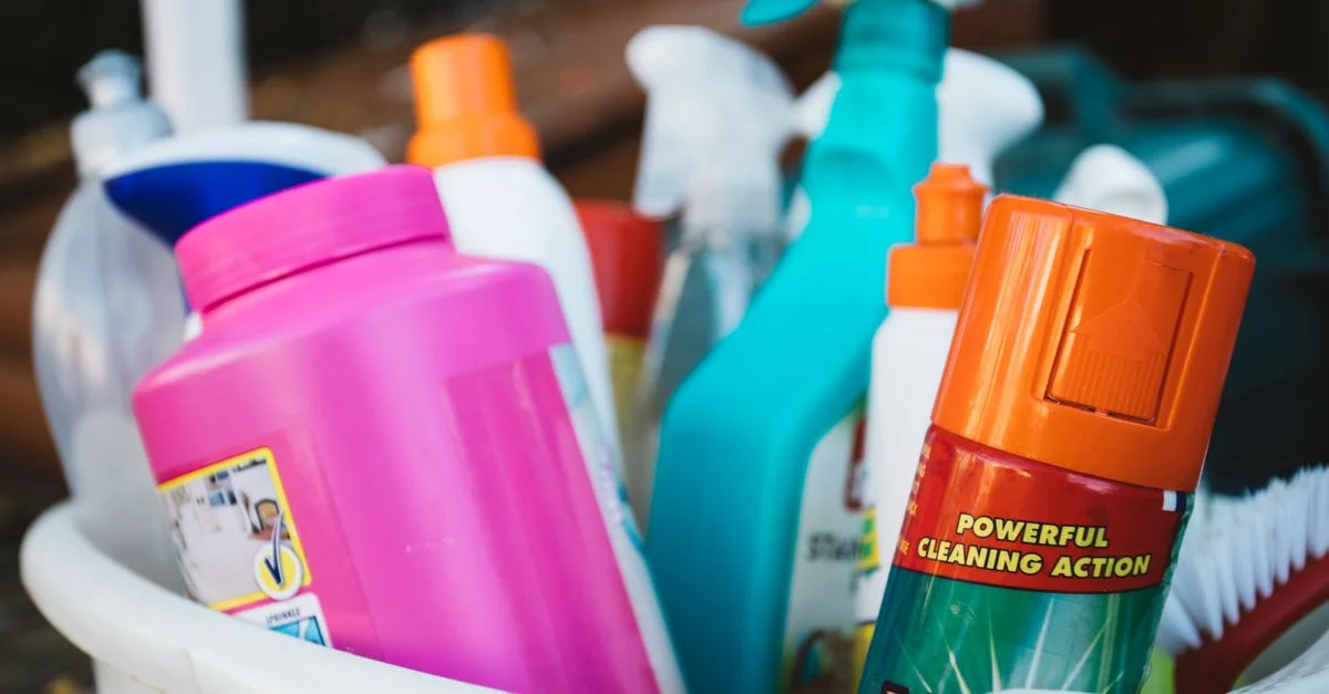 Gros plan sur divers produits de nettoyage dans un seau à l'extérieur, mettant en avant différents détergents et sprays.