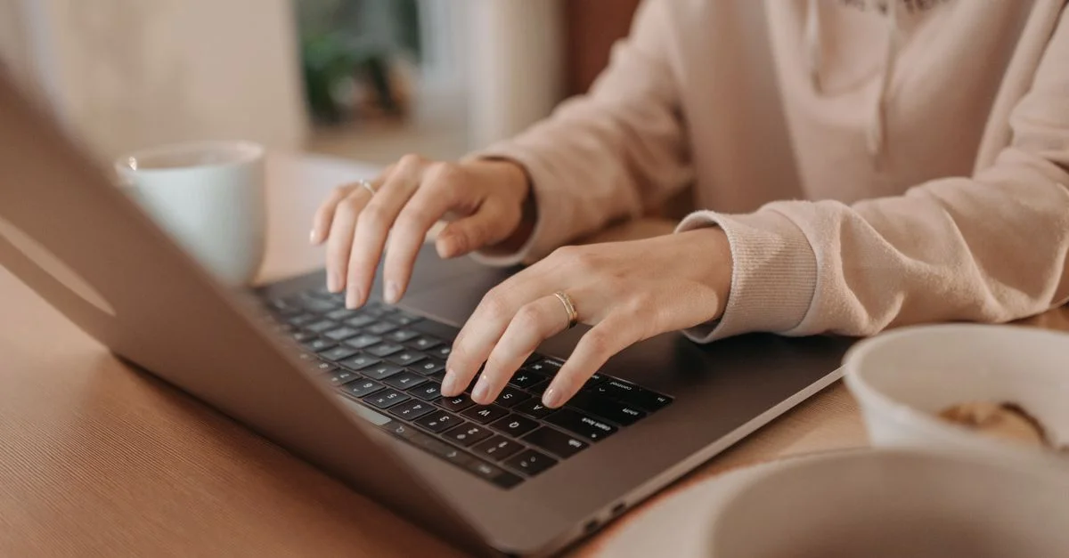 Gros plan d'une femme tapant sur un ordinateur portable à la maison, mettant en avant le télétravail et la technologie.