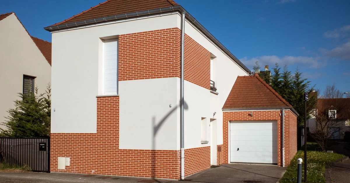 Une maison contemporaine en banlieue avec une façade en brique rouge et blanche dans un cadre de quartier ensoleillé.