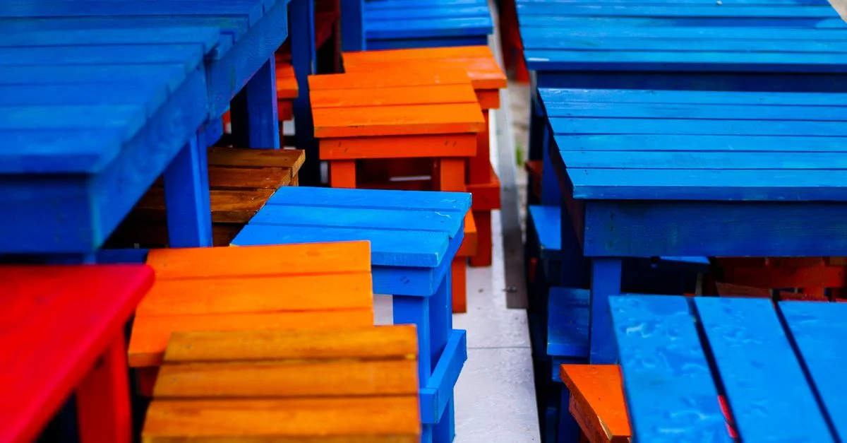 Gros plan sur des tables et tabourets en bois vibrants présentant un mélange de couleurs bleu, orange et rouge.