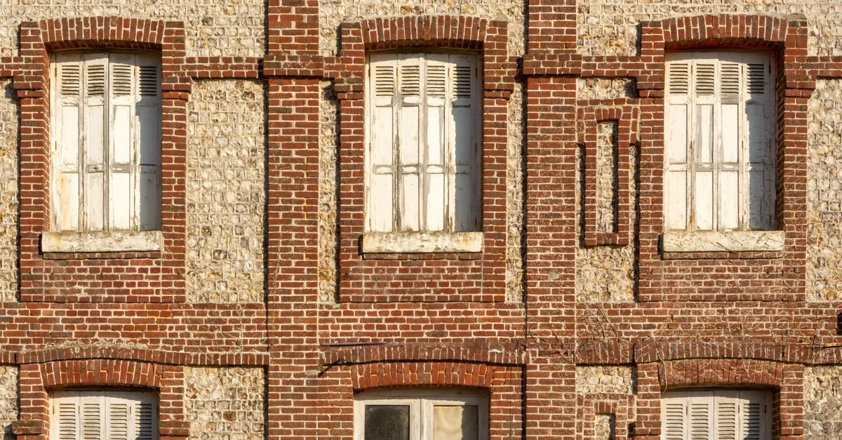 Ancienne façade de bâtiment en brique avec fenêtres à volets en Normandie, France.