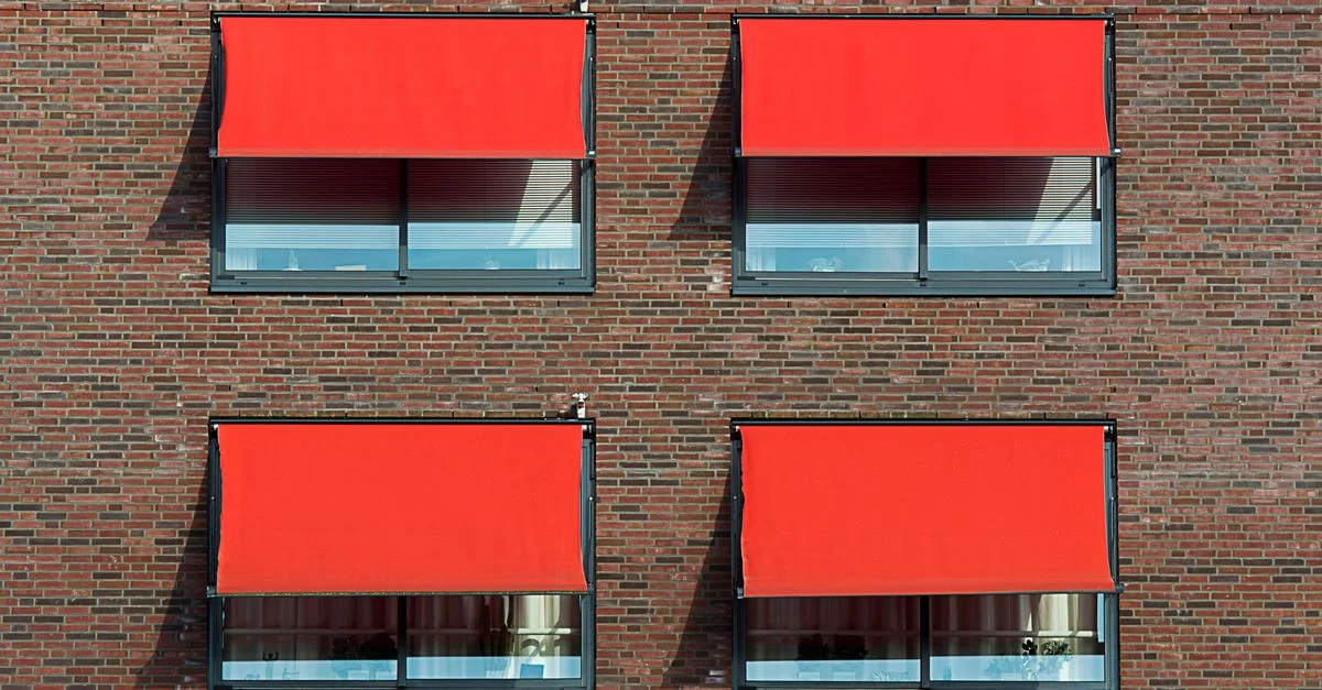 Mur en briques symétrique avec quatre stores rouges couvrant les fenêtres.