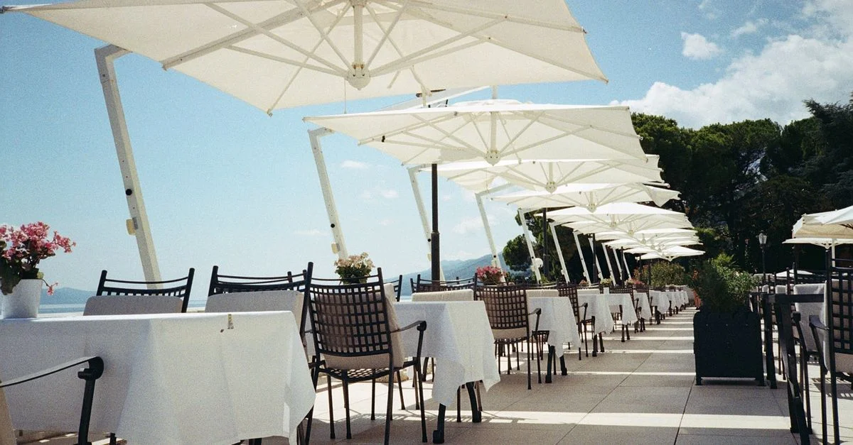 Terrasse de restaurant en bord de mer avec des parasols blancs et des tables vides, une journée d'été parfaite.