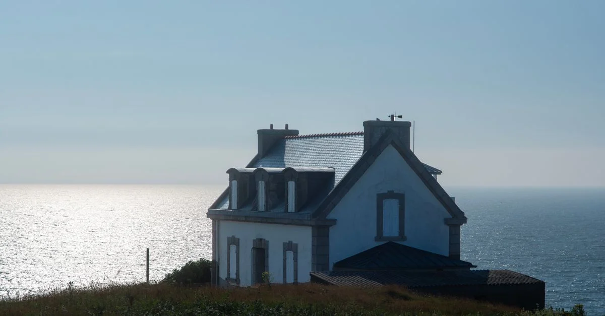 Vue côtière paisible avec une maison au bord de la mer, baignée de soleil.
