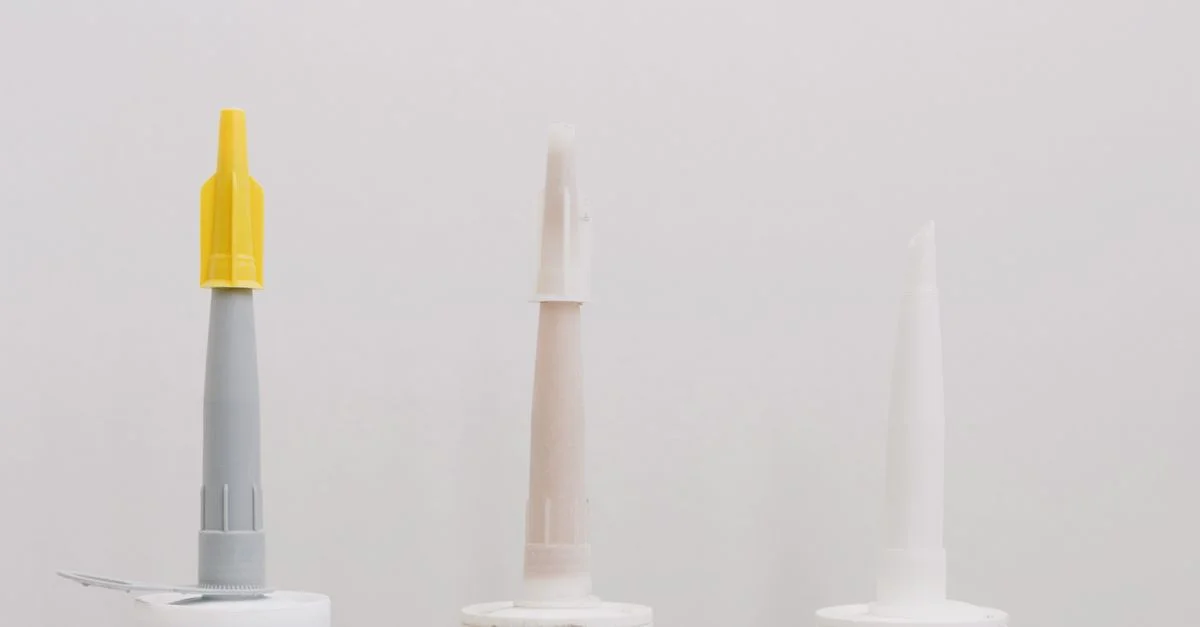 Trois tubes de colle pour construction avec des capuchons colorés sur un fond blanc.