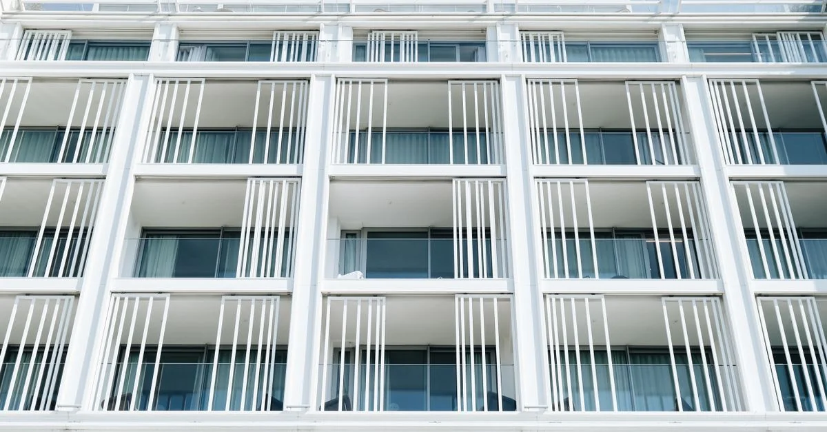 Gros plan sur la façade d'un immeuble d'appartements moderne, blanc, avec des lignes verticales et des fenêtres en verre.