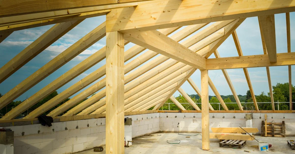 Site de construction inachevé avec un accent sur les fermes de toit en bois sous un ciel dégagé.