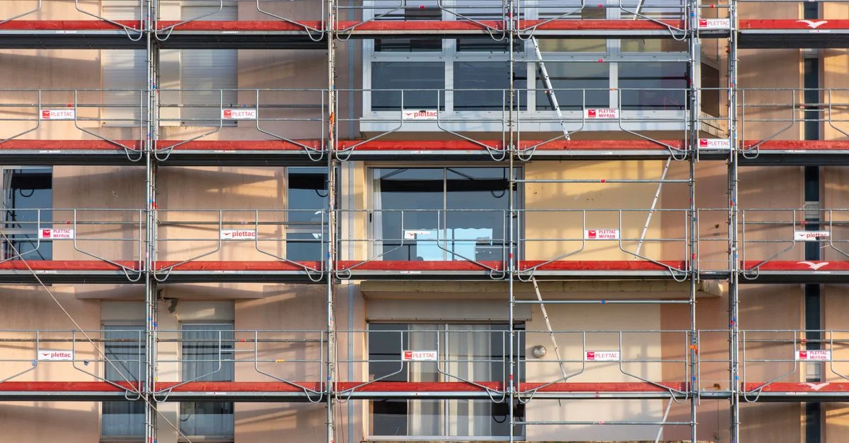 Des échafaudages recouvrent la façade d'un immeuble urbain, révélant les détails d'un chantier de construction.