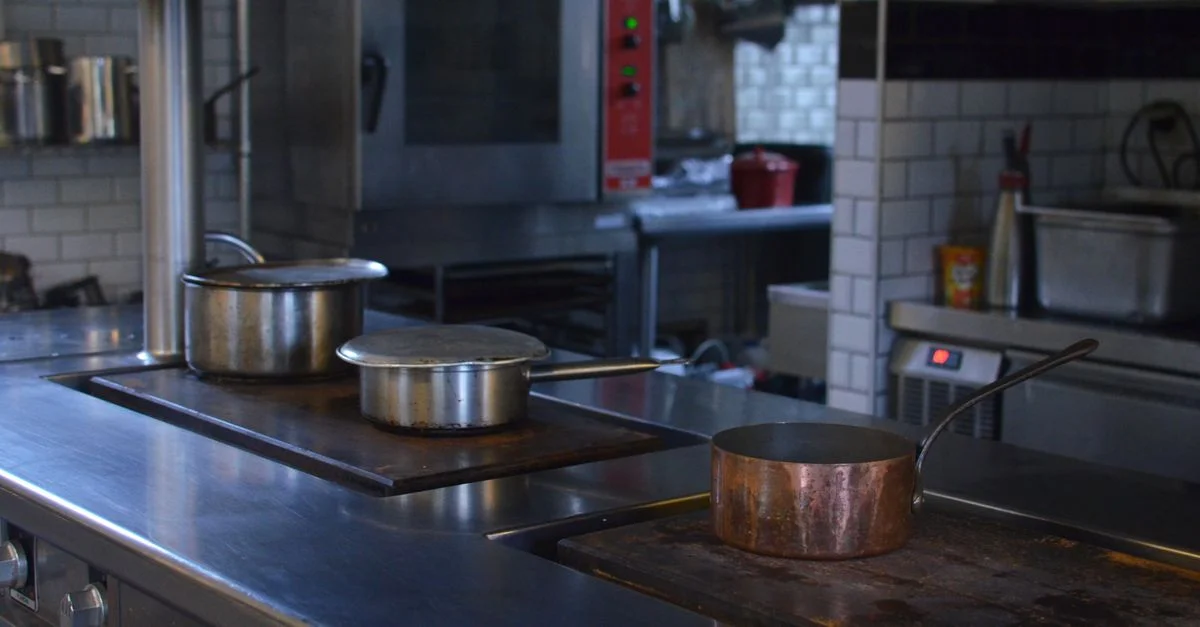 Des casseroles en acier inoxydable sur un comptoir de cuisine dans un cadre de restaurant professionnel.