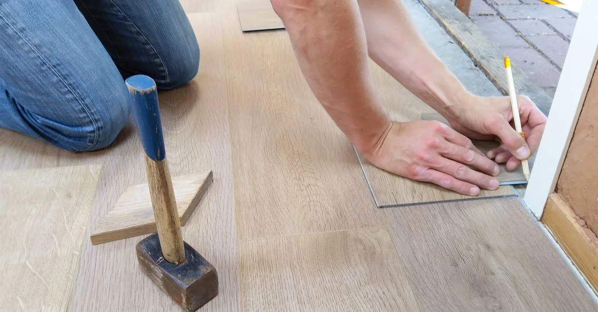 Un artisan mesure et marque soigneusement des panneaux de sol en bois pour une installation précise.