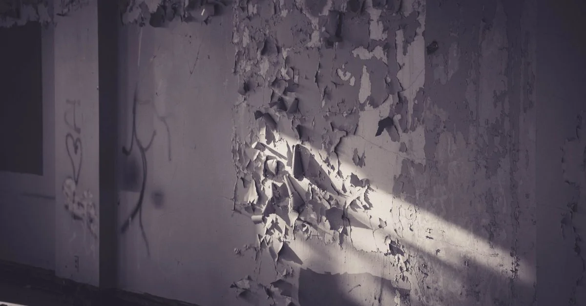 Une lumière dramatique met en valeur la peinture écaillée sur un mur abandonné, créant une atmosphère mélancolique et étrange.