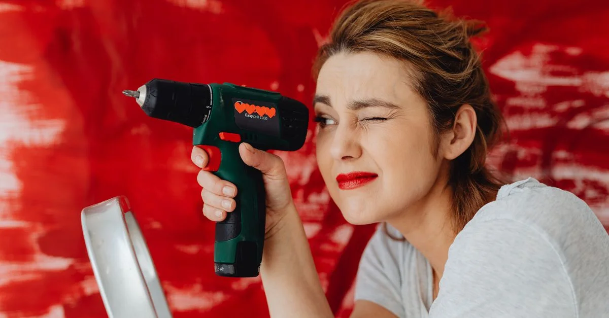 Une femme confiante posant avec une perceuse électrique sur un fond rouge audacieux.