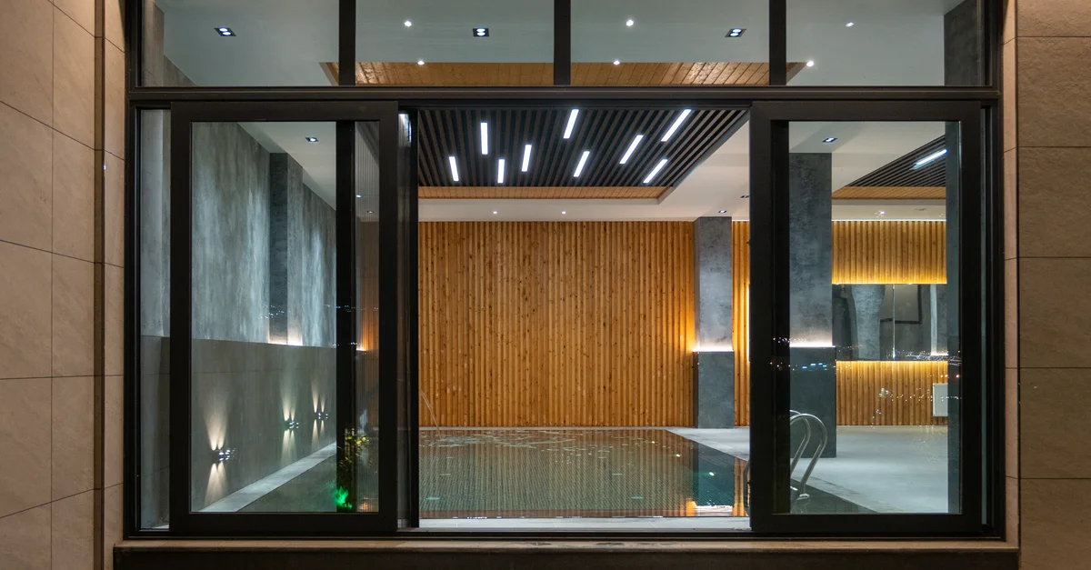 Espace piscine intérieur élégant avec un éclairage moderne, des panneaux en bois et de grandes fenêtres en verre pour la détente.
