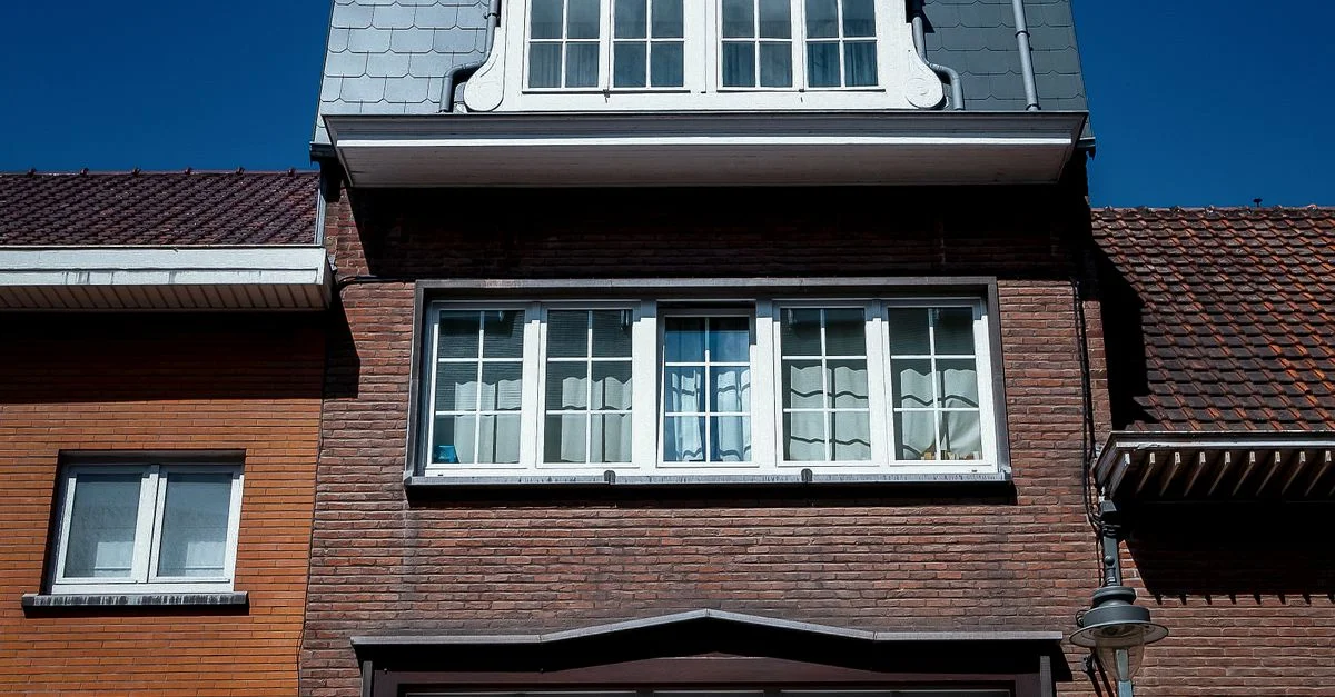Vue rapprochée d'une façade de maison traditionnelle en briques avec des lucarnes sous un ciel bleu clair.