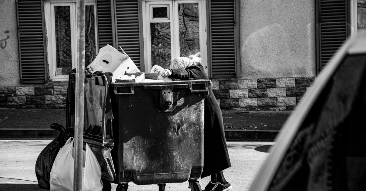 Une femme interagit avec une benne sur une rue, une scène urbaine en noir et blanc à ciel ouvert.