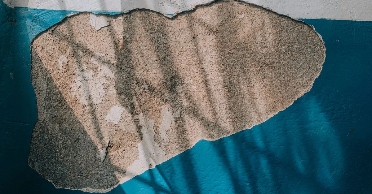 Vue détaillée d'un mur avec de la peinture bleue écaillée et du plâtre exposé, montrant des textures et des ombres.