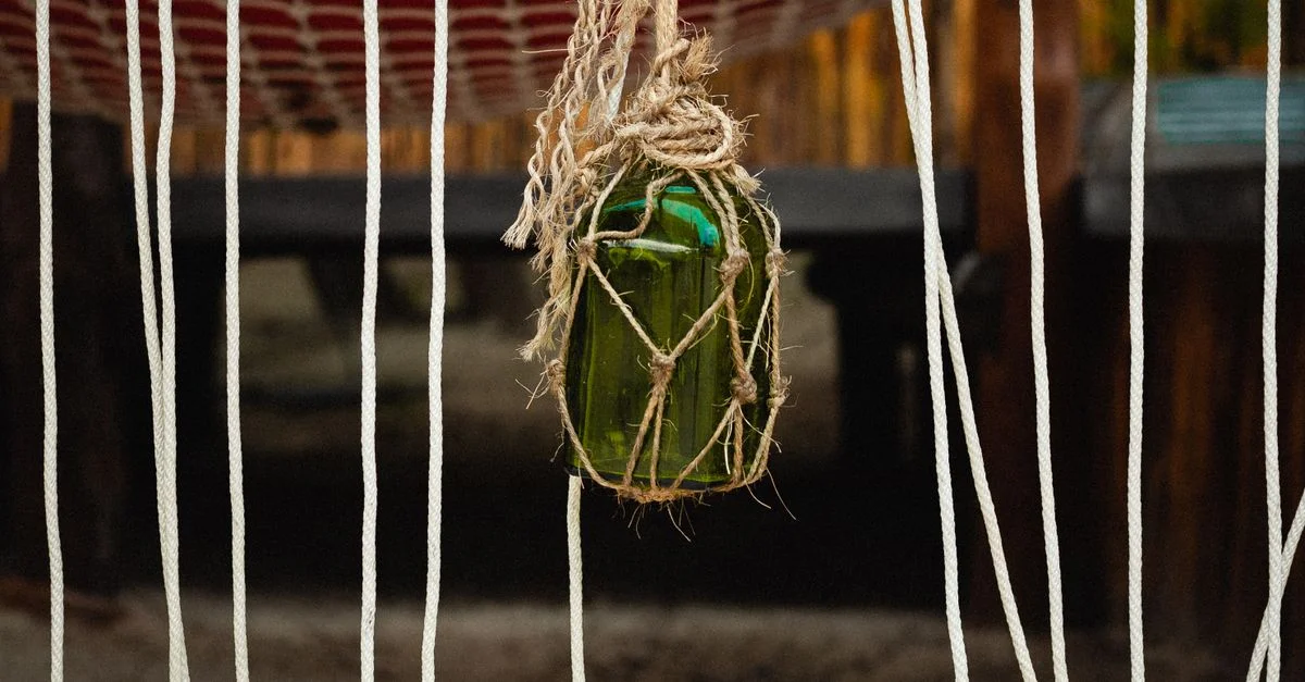 Une bouteille en verre verte artistiquement enroulée dans de la corde pend à l'extérieur devant un fond rustique.