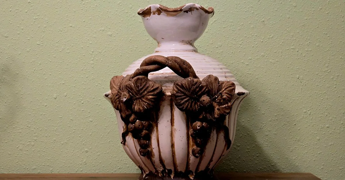 Vase en céramique blanc classique avec un design floral rustique sur une étagère en bois contre un mur pastel.