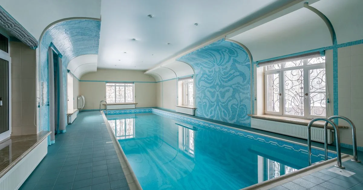 Grande piscine intérieure avec un beau design en carrelage bleu et un éclairage naturel.